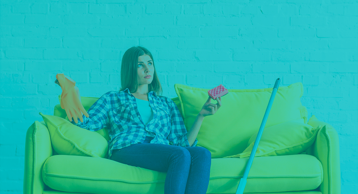 Mulher no sofá verde claro com luva de limpeza e escova de cabelo, rodo ao lado