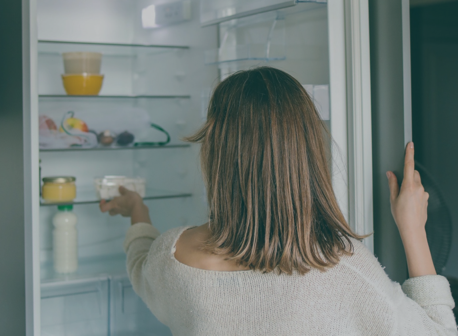 Mulher de costas a abrir frigorífico branco com alimentos variados dentro