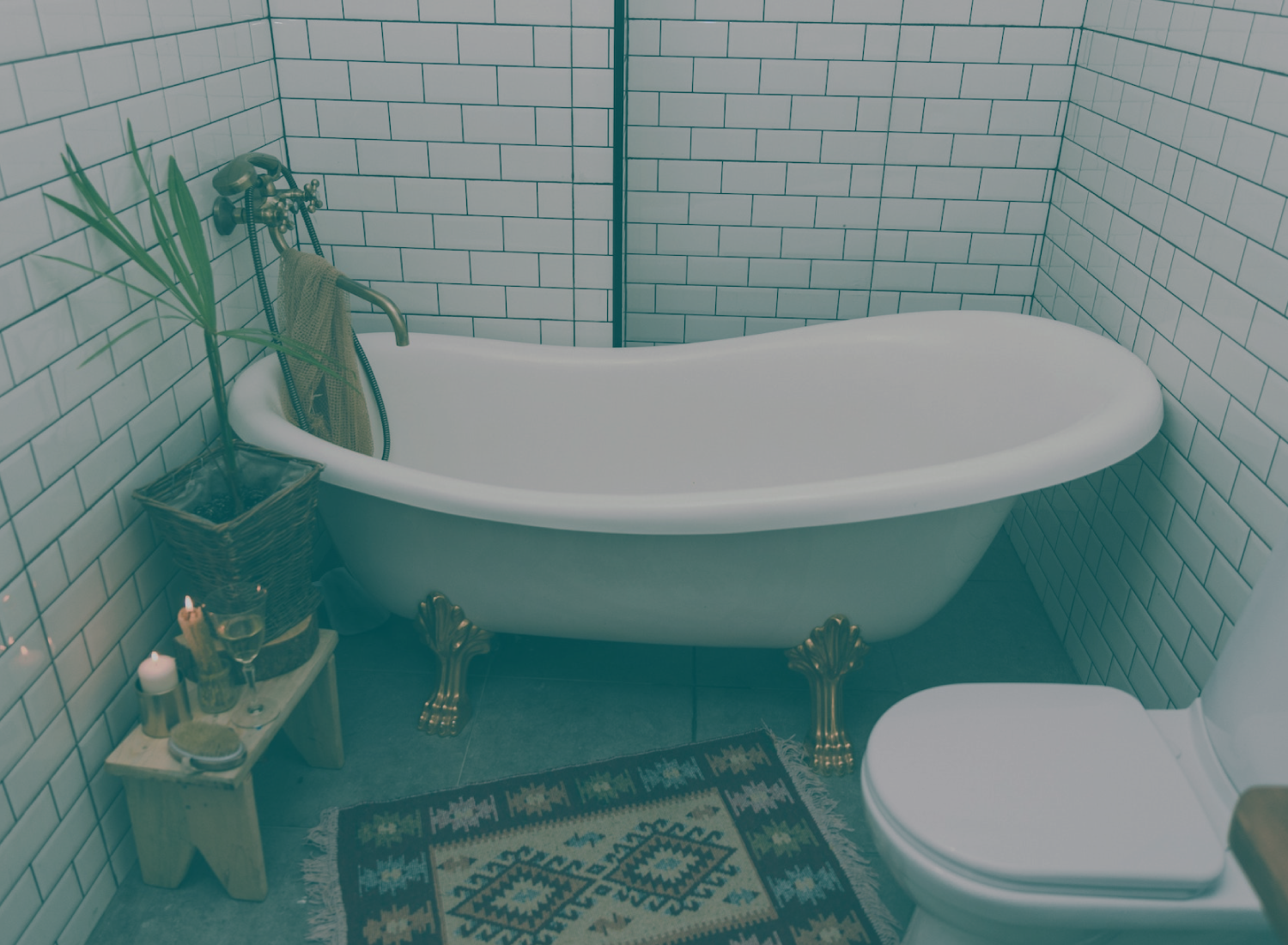 Banheira branca vintage com pés dourados num banheiro com azulejos brancos e tapete decorativo