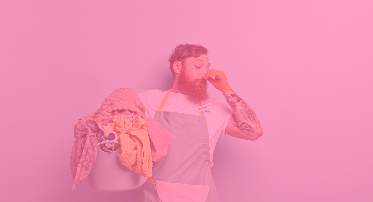 Homem com avental segurando balde com roupa em fundo rosa