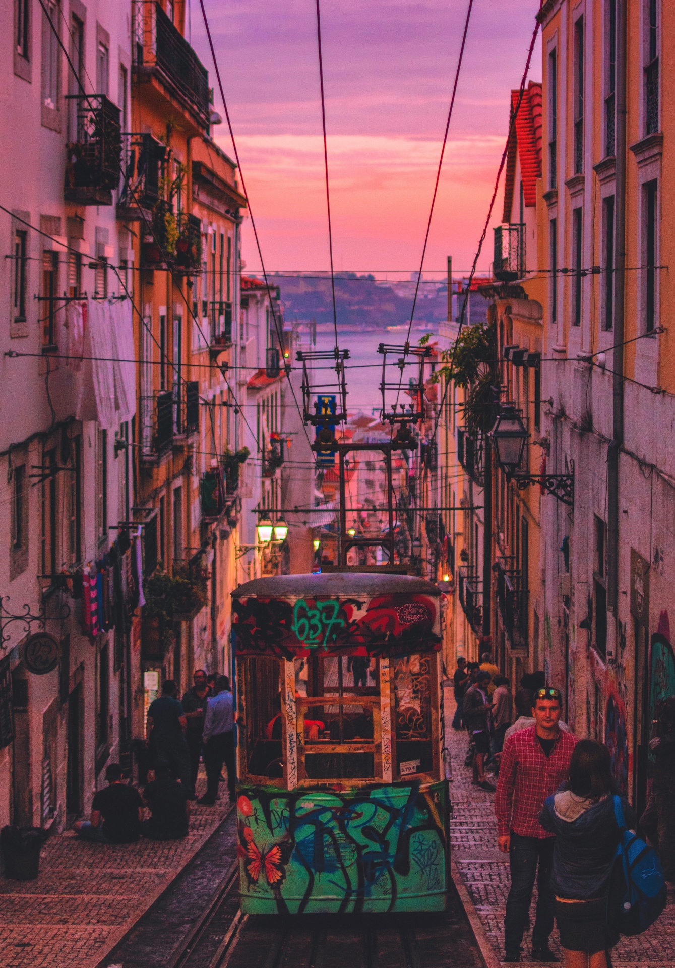 Bonde colorido a descer rua íngreme com edifícios antigos e pessoas ao pôr-do-sol