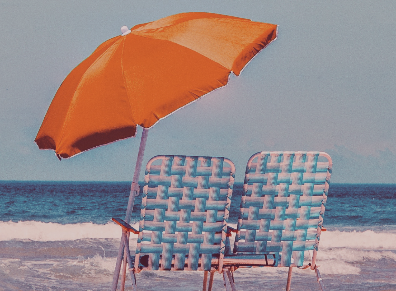 Duas cadeiras de praia azuis entrelaçadas e um guarda-sol laranja numa praia com mar ao fundo