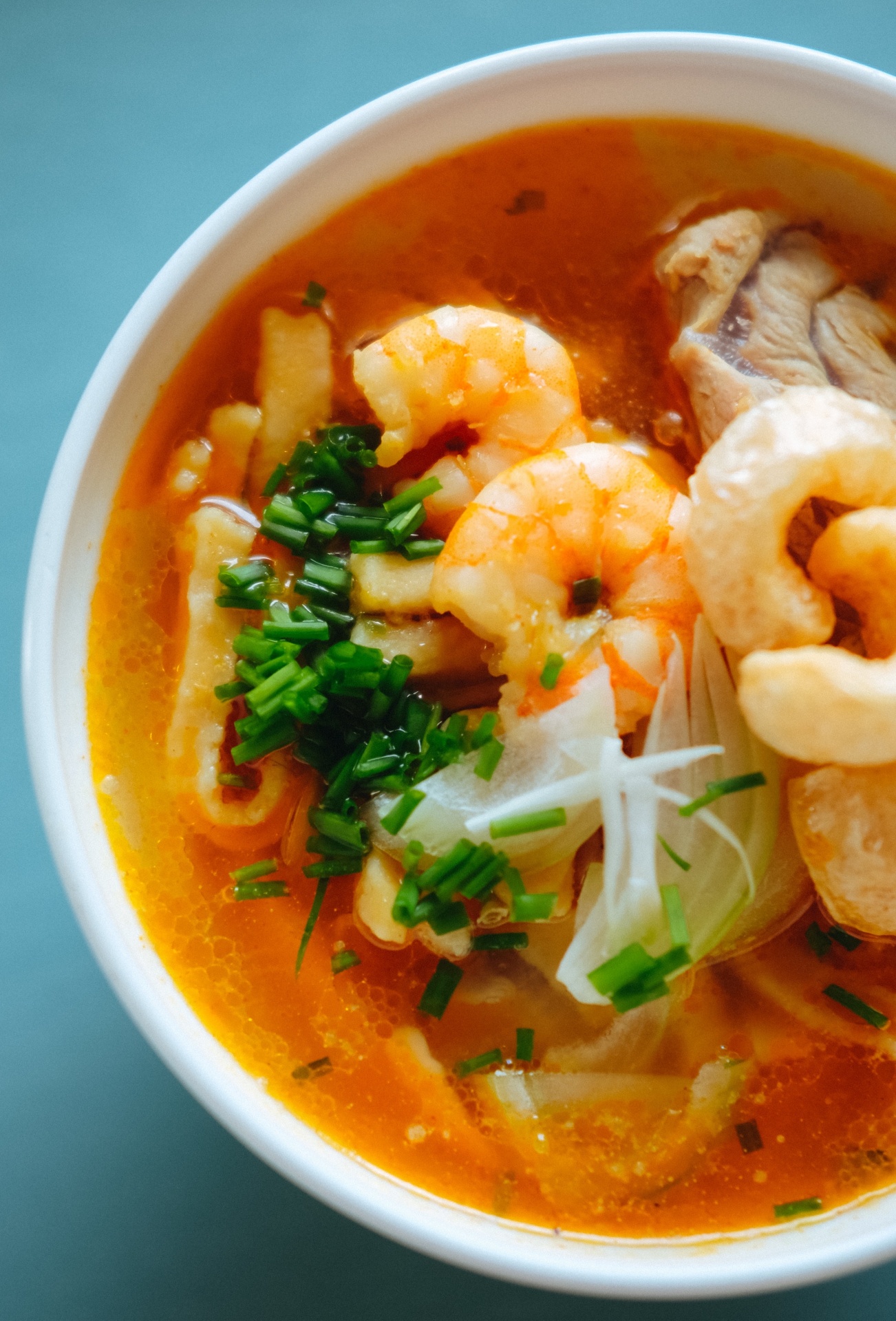 Tigela branca com sopa de camarão, cebolinho e cebola