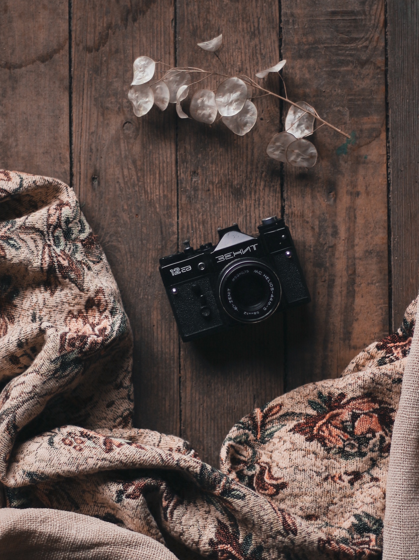 Máquina fotográfica analógica preta sobre tecido floral e madeira