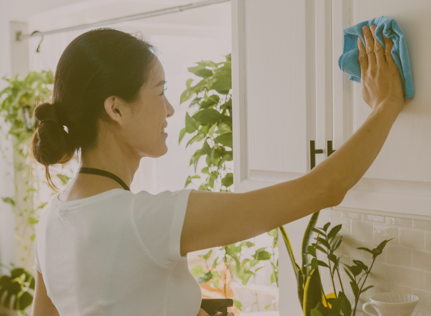 Mulher a limpar armário branco na cozinha com pano azul