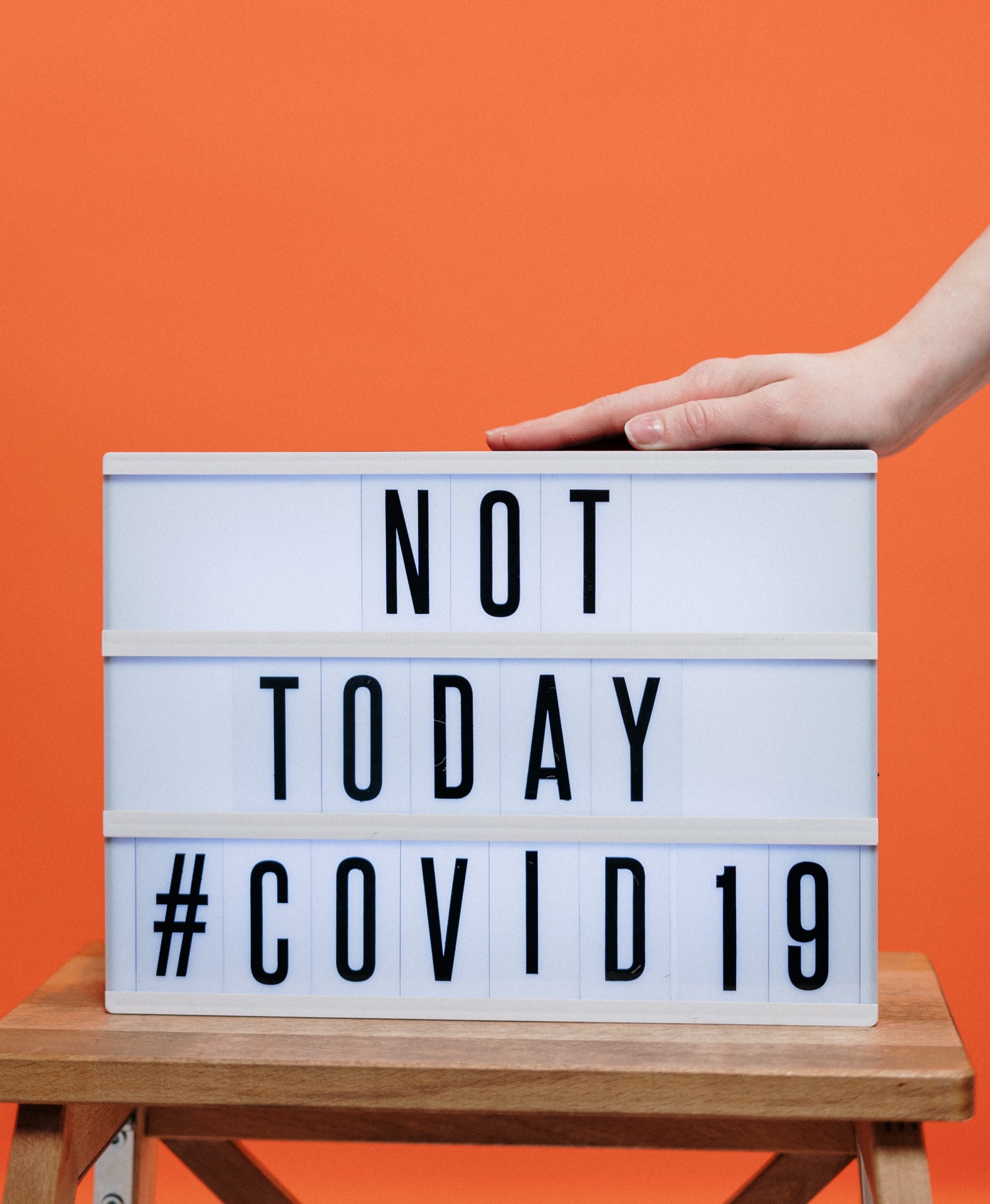 Caixa de luz branca com mensagem NOT TODAY #COVID19 sobre mesa de madeira e fundo laranja