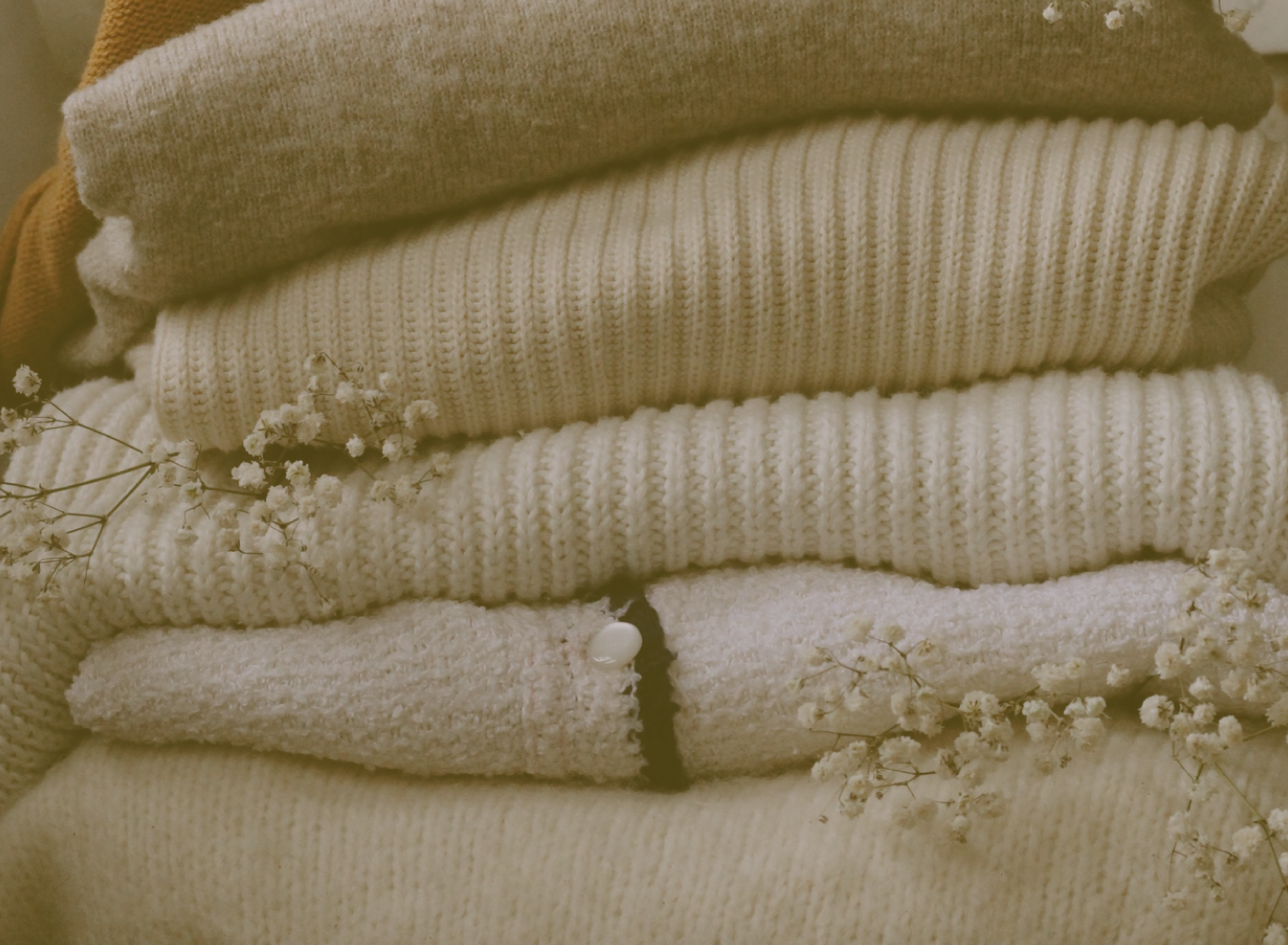 Pilha de roupas de malha em tons neutros com flores secas pequenas