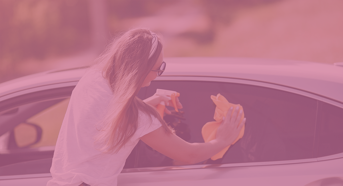 Mulher a limpar janela de carro branco com pano amarelo e spray
