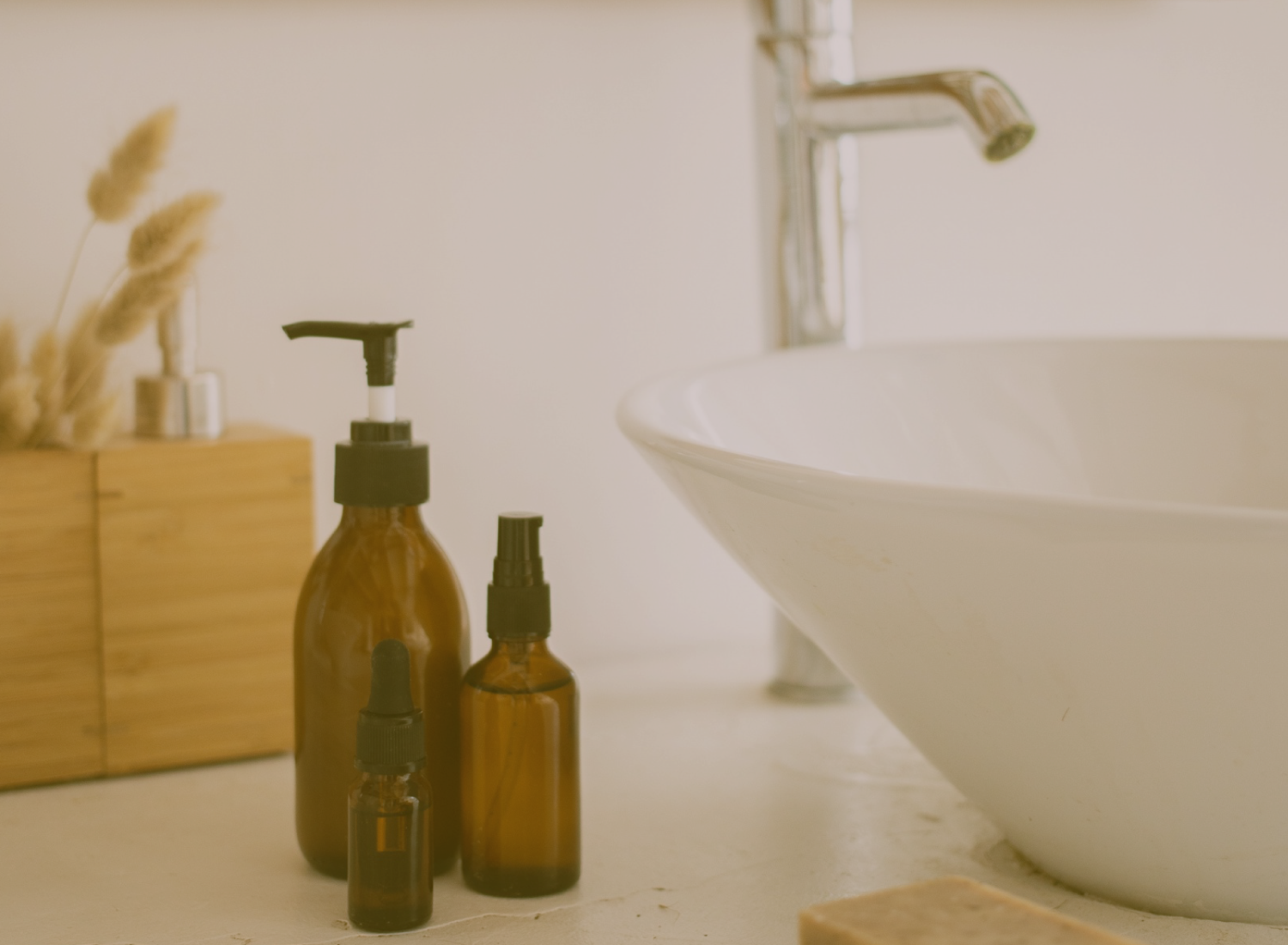 Três frascos âmbar com tampas pretas em cima de uma pia branca com torneira prateada