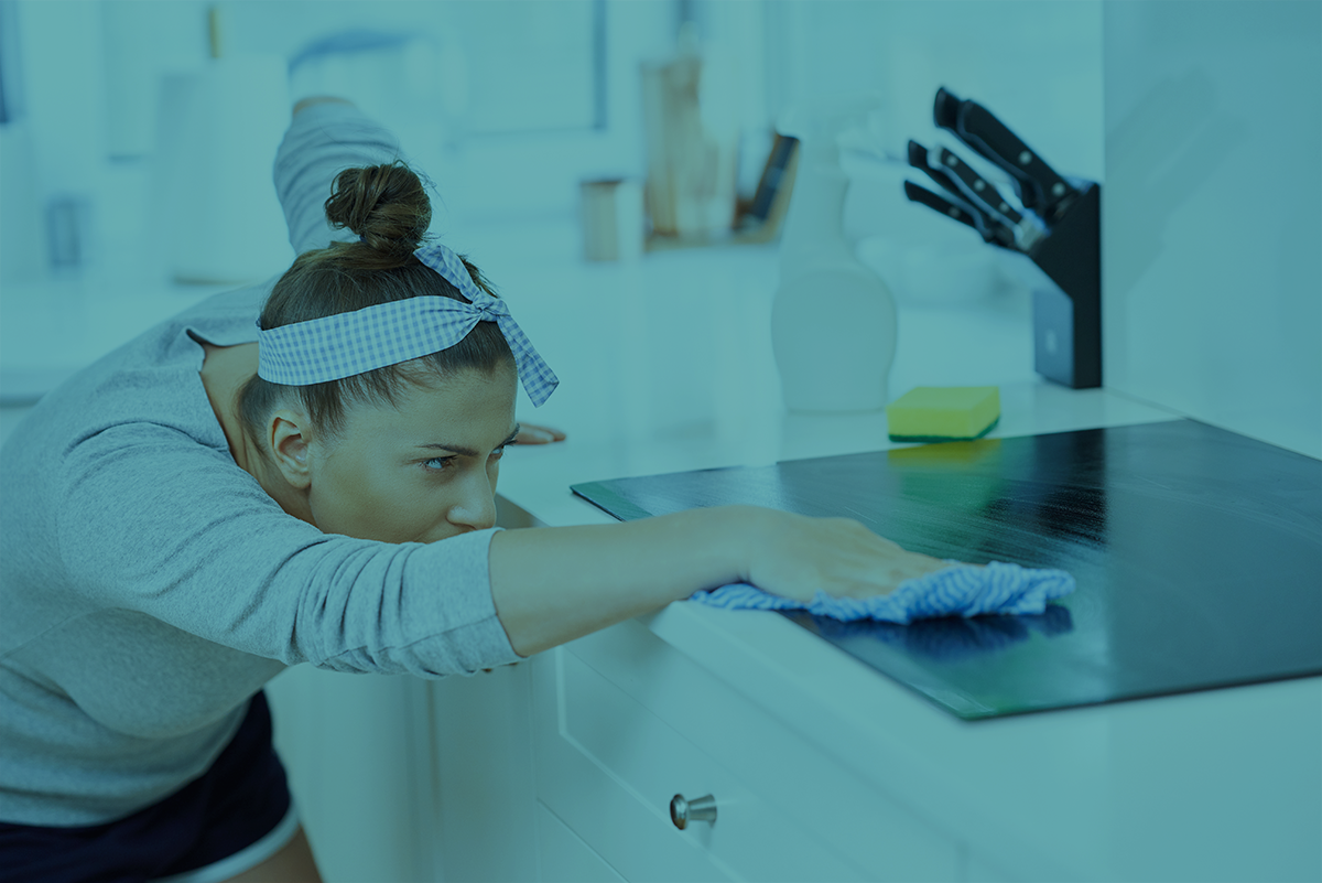 Mulher a limpar placa de fogão preta numa cozinha branca