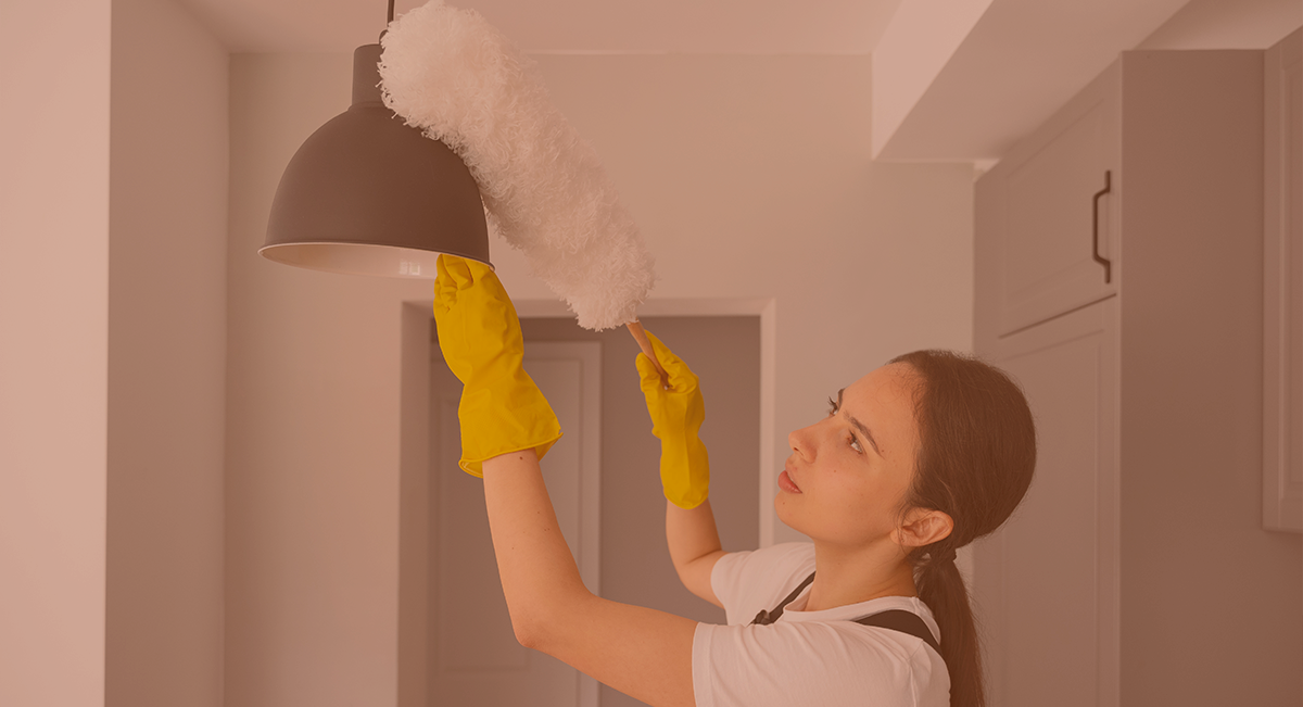 Mulher a limpar candeeiro de teto com luvas amarelas