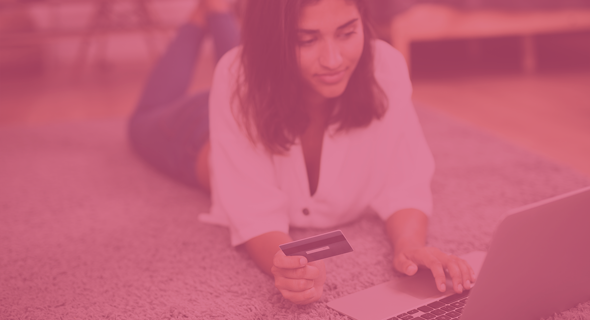 Mulher deitada no tapete a usar portátil e segurando cartão de crédito