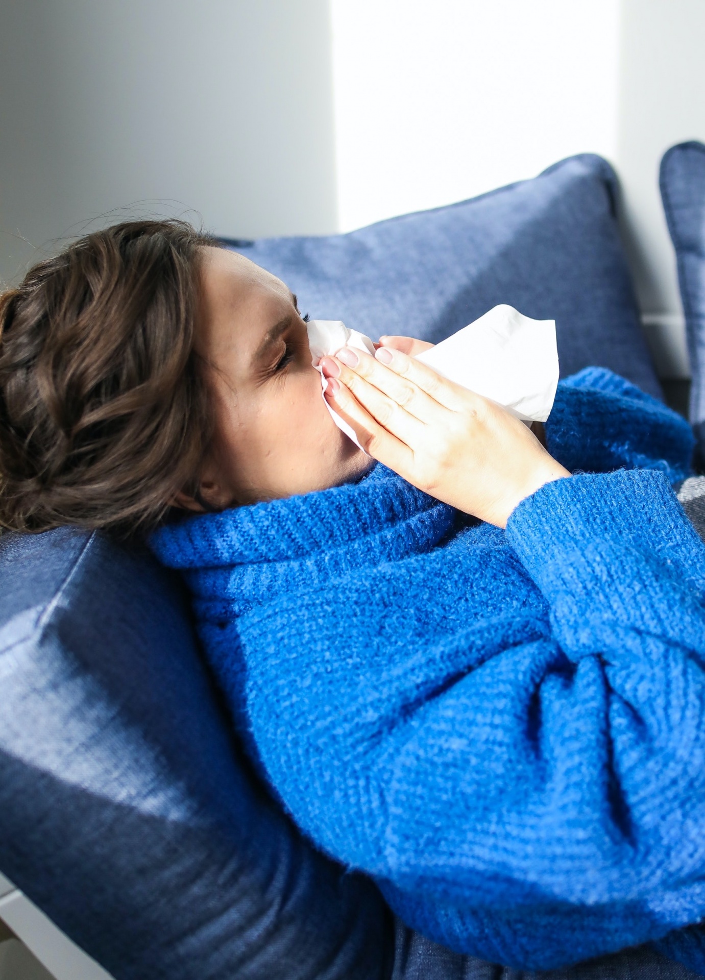 Pessoa com camisola azul a deitar num sofá azul claro com lenço no rosto