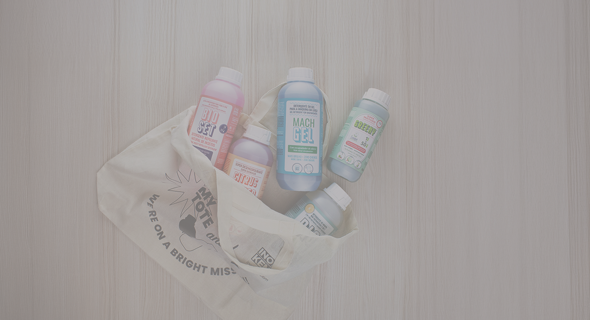 Cinco frascos de geles e loções coloridos dentro de bolsa de pano sobre mesa de madeira clara