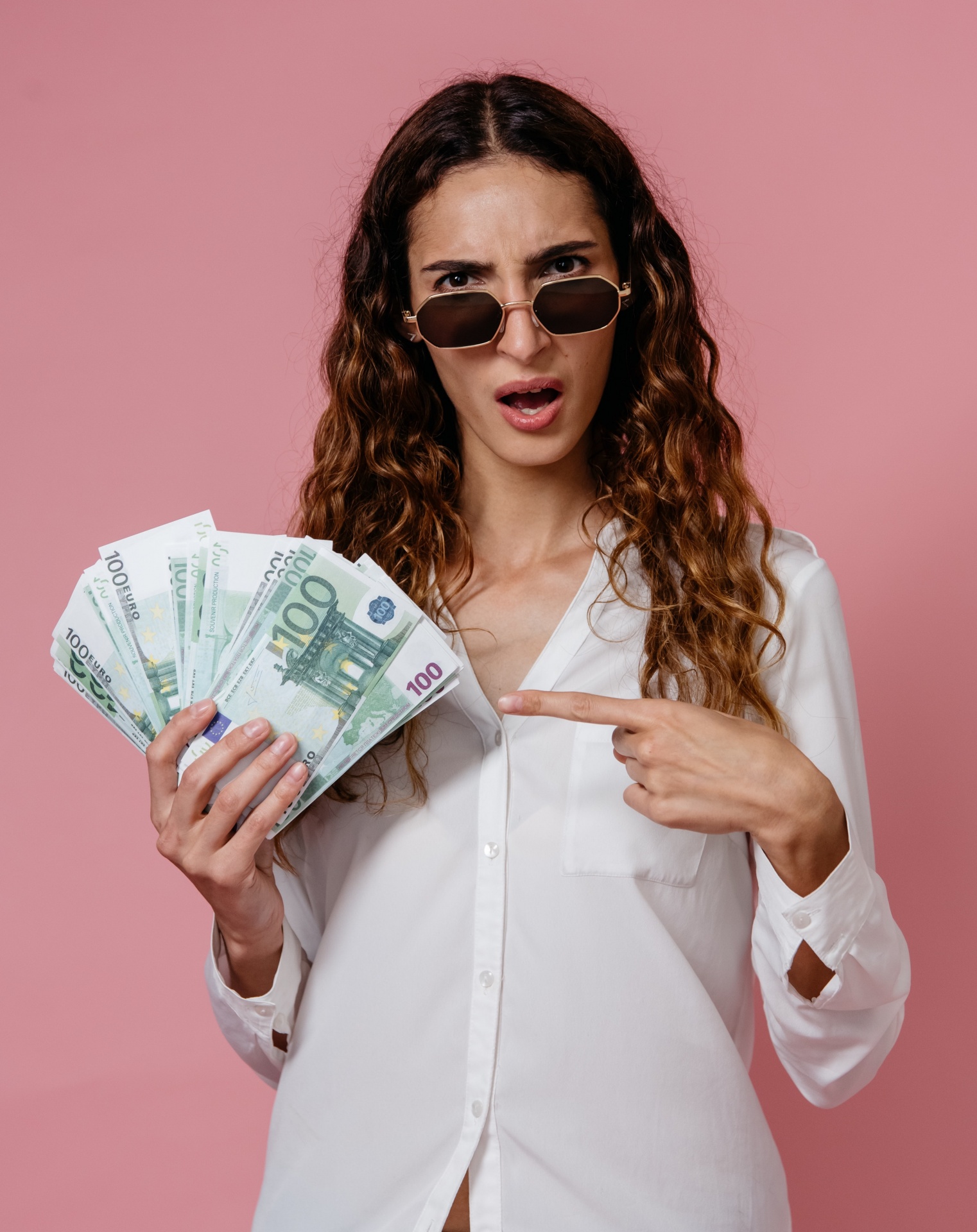 Mulher com óculos de sol e camisa branca segurando notas de 100 euros em leque