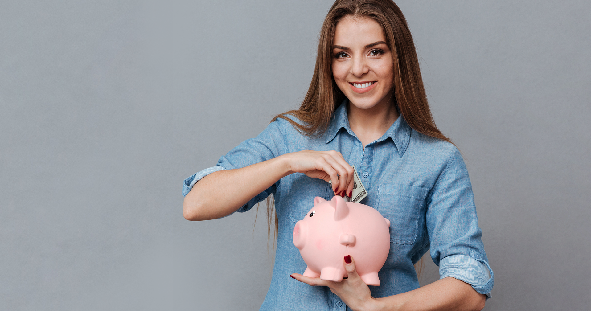 Mulher com camisa azul segurando mealheiro de porco rosa colocando moedas