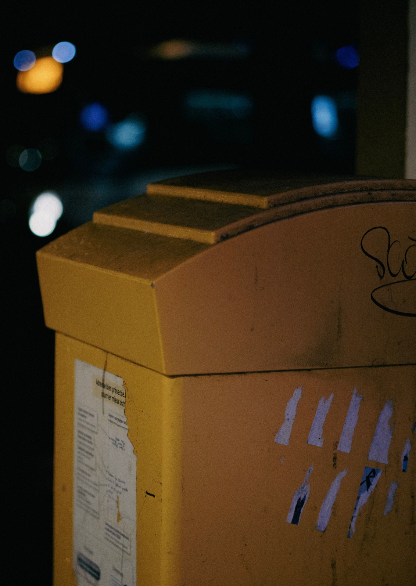 Ecoponto amarelo: dúvidas e dicas Caixa postal amarela de metal com autocolantes e papel adesivo, vista à noite.