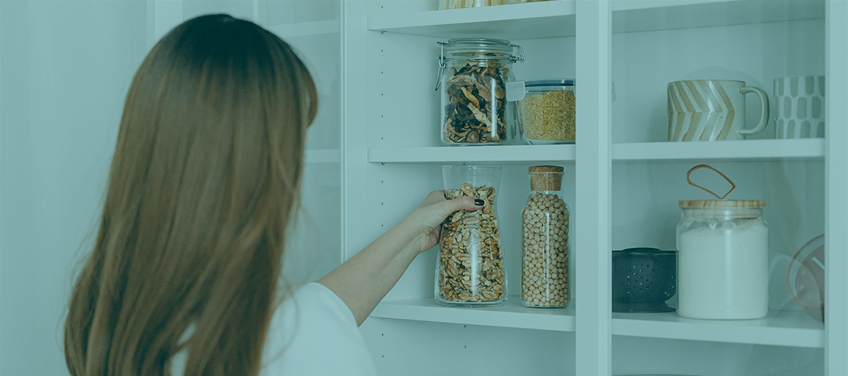 Pessoa a colocar frasco com cereais em estante branca com frascos, canecas e açúcar