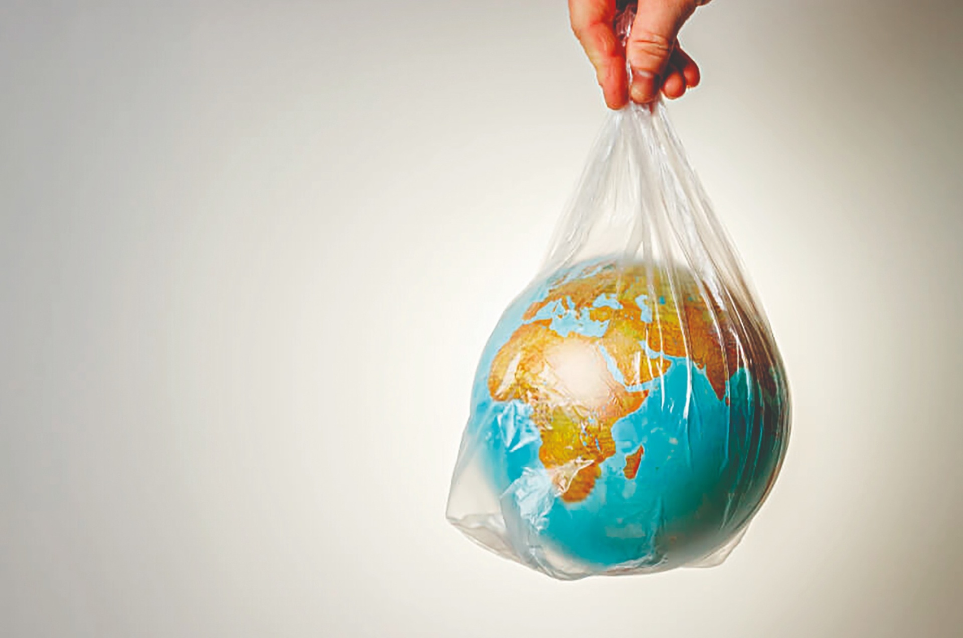 Globo terrestre colorido dentro de um saco plástico transparente segurado por uma mão