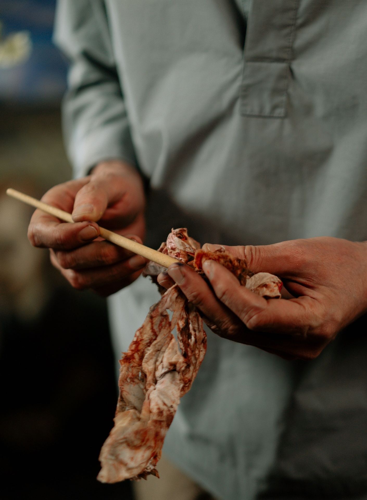 Mãos segurando pauzinho de madeira e tecido manchado com camisa cinza