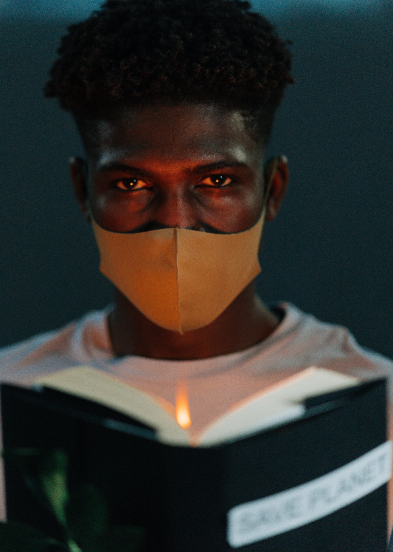 Homem com máscara bege lendo livro com capa preta e texto 'SAVE PLANET'