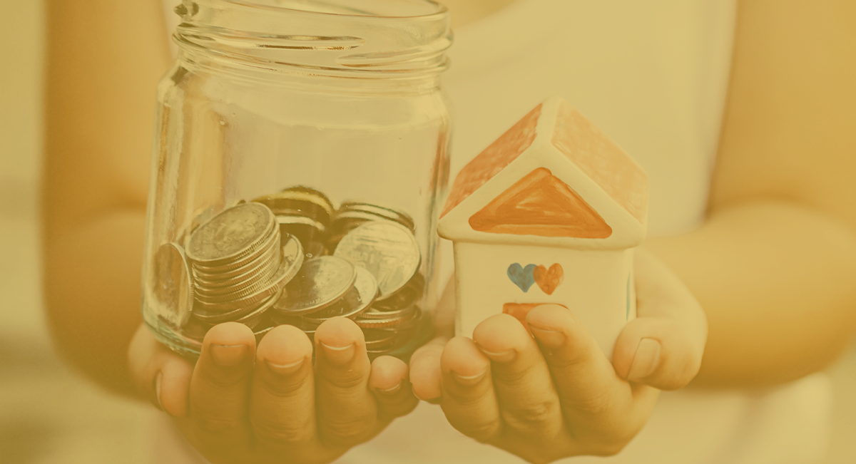 Mãos segurando um frasco com moedas e uma casa em miniatura branca com corações