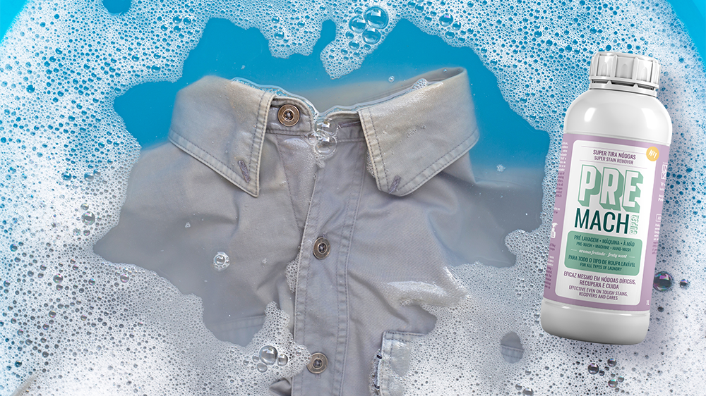 Camisa cinza clara sendo lavada com espuma de sabão azul e branco ao lado um frasco branco PRE MACH