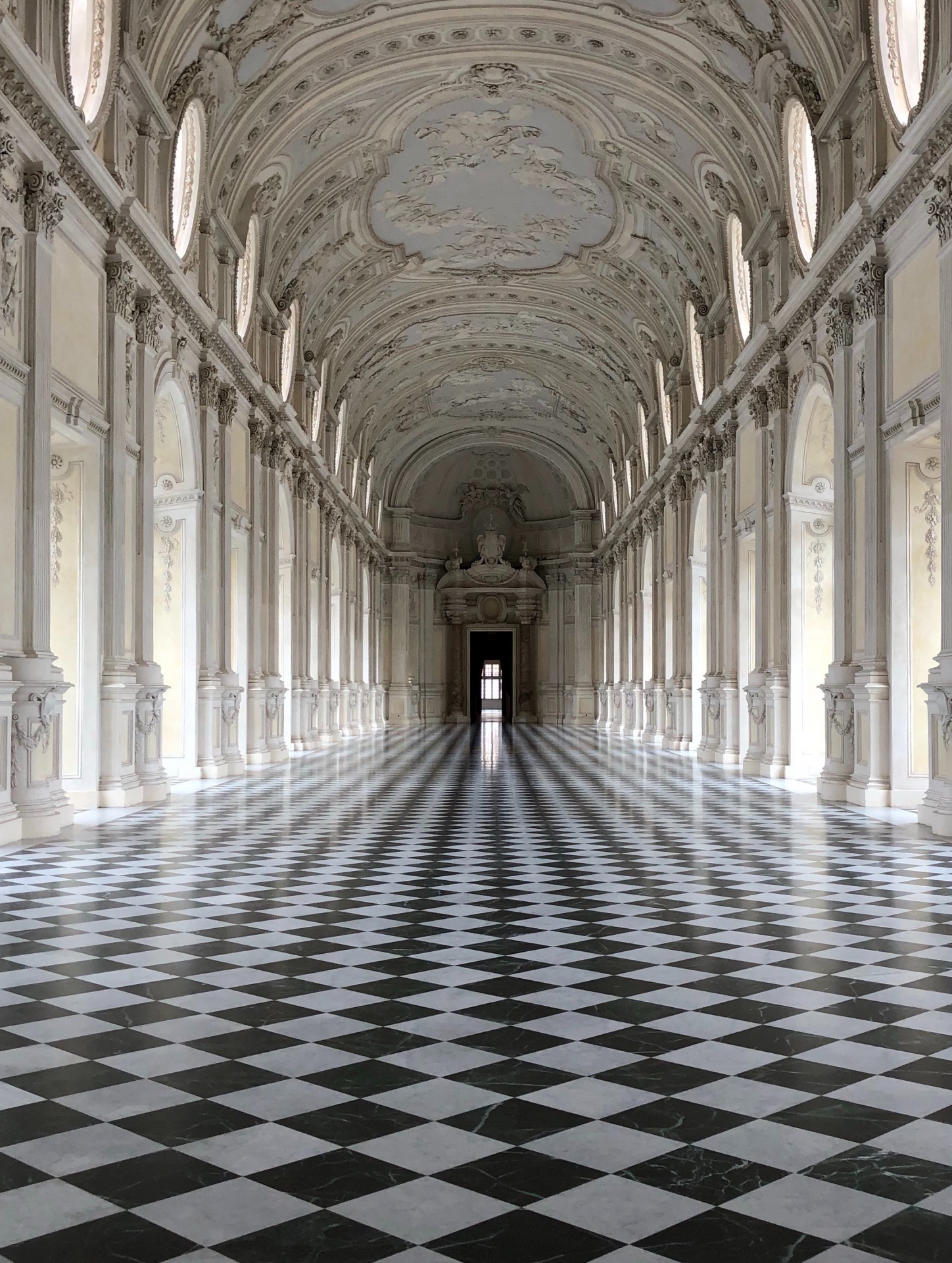 Corredor longo com chão xadrez, colunas e teto ornamentado