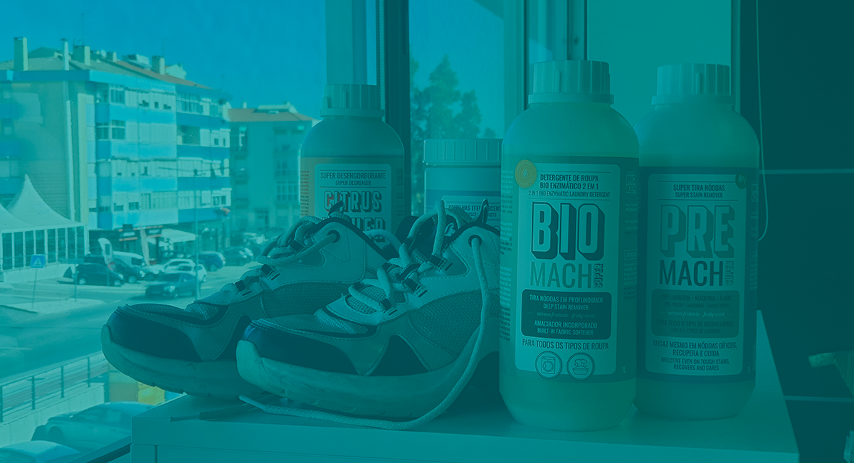 Ténis cinza e azul ao lado de três frascos brancos de produtos de limpeza em cima de uma mesa com vista para prédios ao fundo