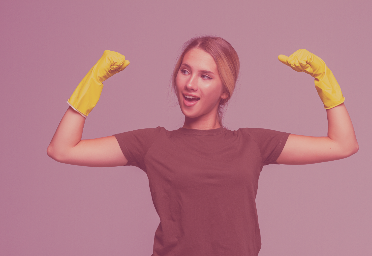 Mulher com t-shirt castanha e luvas amarelas flexionando os braços num fundo rosa