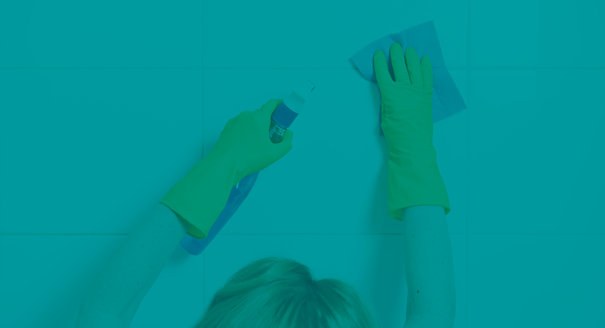 Pessoa limpando azulejos brancos com luvas verdes e spray de limpeza