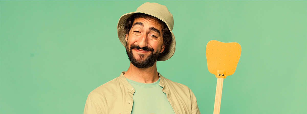 Homem com chapéu bege segurando utensílio de cozinha amarelo em fundo verde