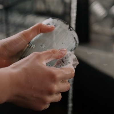 Mãos a lavar um copo de vidro com espuma sob água corrente