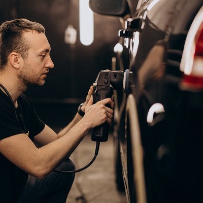 Homem a polir um carro preto com uma máquina polidora elétrica