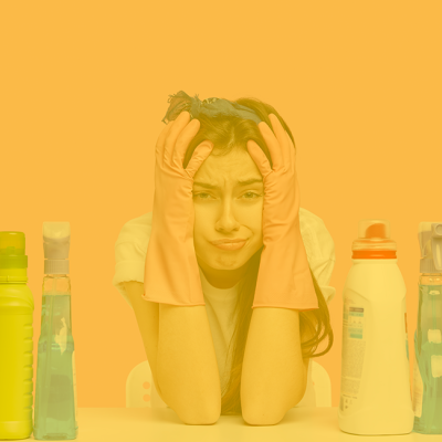 Mulher com luvas de borracha entre várias garrafas de limpeza coloridas sobre mesa com fundo amarelo