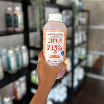 Frasco de produto de limpeza Citrus Power com etiqueta laranja e branca segurado por mão frente a prateleiras