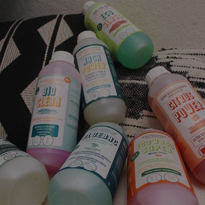 Seis garrafas de detergentes líquidos coloridos com rótulos em português numa superfície branca