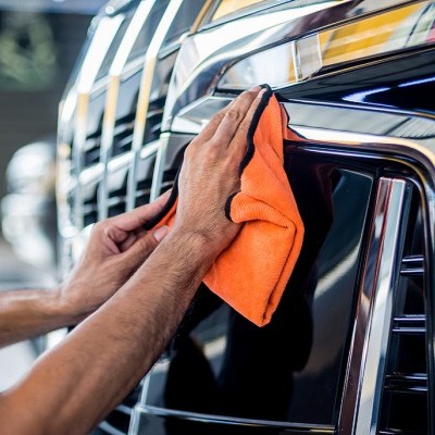 Mãos a limpar carro com pano laranja