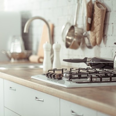 Bancada de cozinha com fogão de gás, chaleira, utensílios pendurados e armários brancos