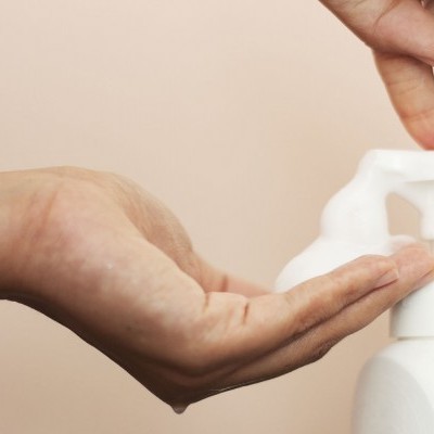 Mãos a usar dispenser de espuma branco em fundo bege claro