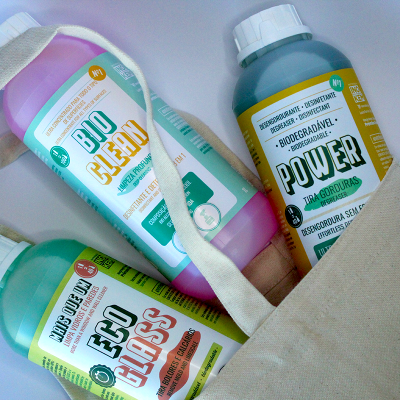 Três garrafas coloridas de produtos de limpeza ecológicos dentro de uma bolsa de tecido crú