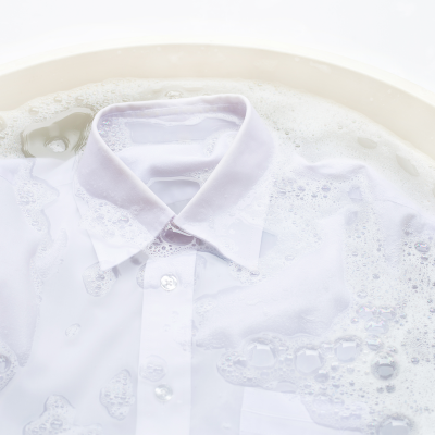 Camisa branca de botão submersa em água com espuma dentro de uma bacia.