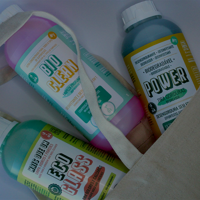 Três frascos coloridos de produtos de limpeza biodegradáveis dentro de saco de tecido cru.