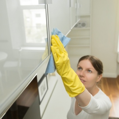 Mulher a limpar armário branco com pano azul e luvas amarelas