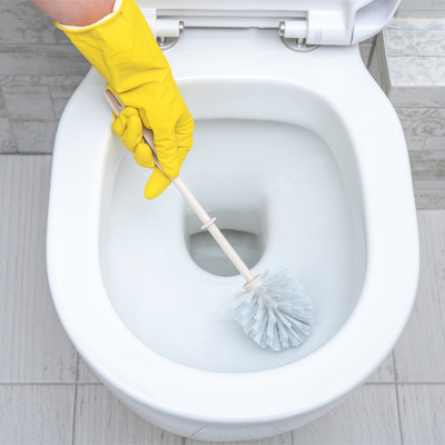Pessoa a limpar sanita branca com escova e luva amarela
