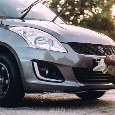 Carro Suzuki cinzento metalizado com homem a limpar na frente ao ar livre