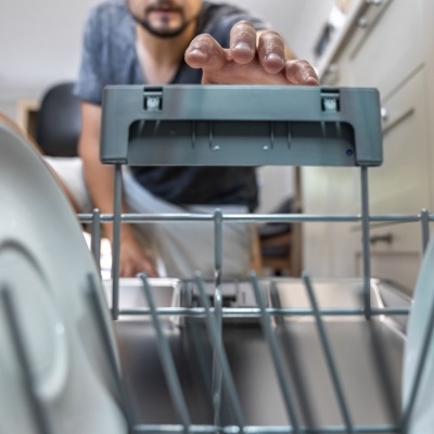 Homem a encher máquina de lavar loiça com pratos.