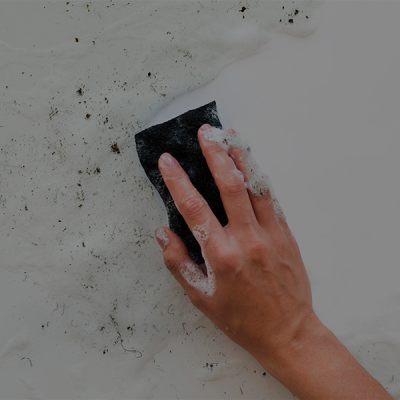 Mão segurando esponja preta a limpar superfície branca suja