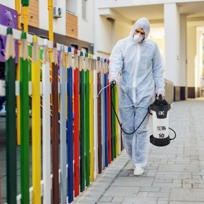 Pessoa a desinfetar passeio junto a vedação colorida em área urbana