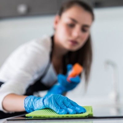 Pessoa a limpar superfície preta com pano verde e luvas azuis numa cozinha moderna